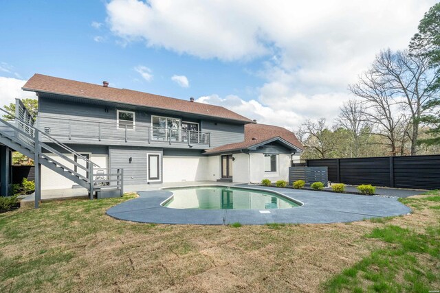 rear view of property featuring fence, stairway, an outdoor pool, and a lawn