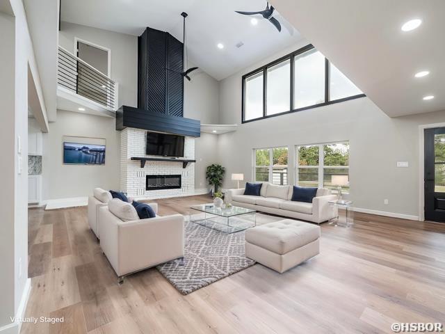 living room with light wood-style flooring, recessed lighting, a high ceiling, a fireplace, and baseboards