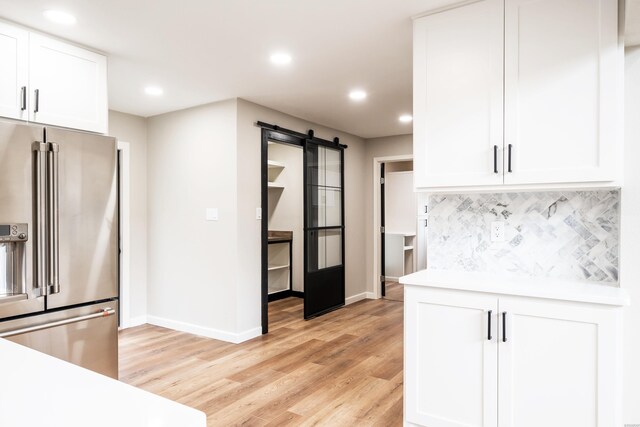 kitchen featuring high quality fridge, a barn door, white cabinetry, light countertops, and backsplash