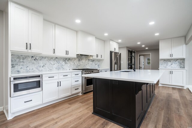 kitchen with a center island with sink, light countertops, white cabinets, a sink, and high quality appliances