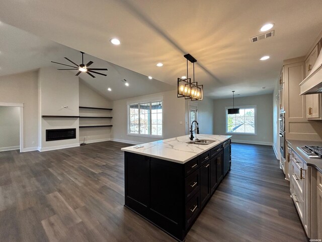 kitchen with pendant lighting, a center island with sink, open floor plan, a sink, and dark cabinets