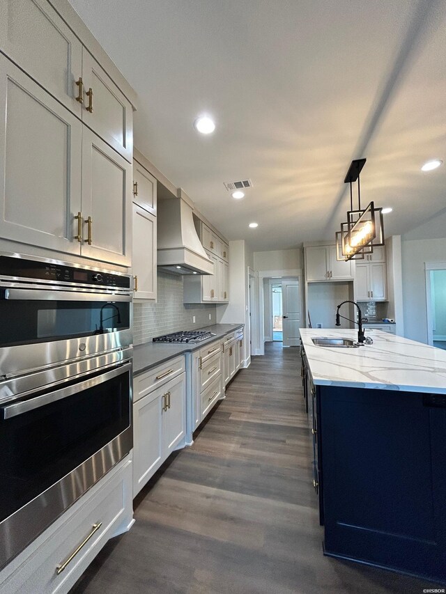 kitchen with a kitchen island with sink, a sink, visible vents, appliances with stainless steel finishes, and custom exhaust hood