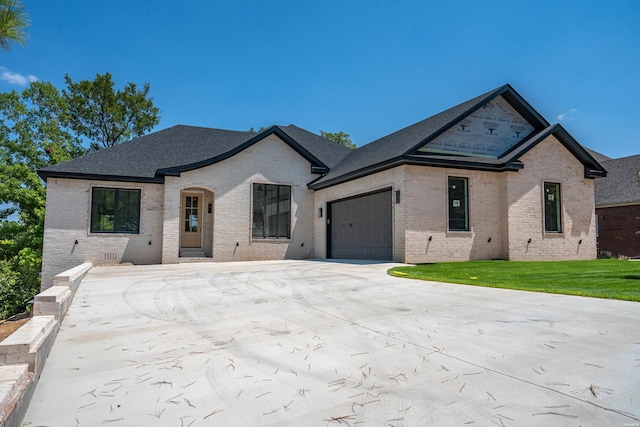 french provincial home featuring an attached garage, driveway, a front lawn, and brick siding