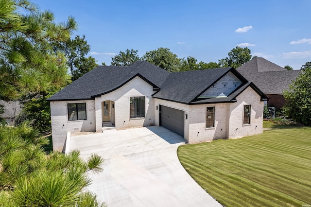 french country home with a shingled roof, concrete driveway, an attached garage, a front yard, and brick siding