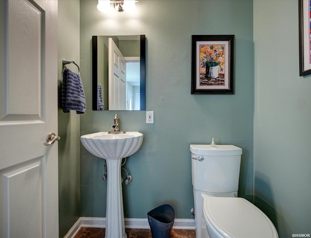 half bath featuring baseboards and toilet