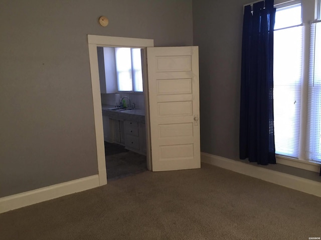 spare room featuring baseboards, dark colored carpet, and a sink