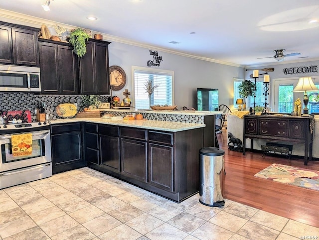 kitchen featuring stainless steel appliances, decorative backsplash, ornamental molding, a ceiling fan, and a peninsula