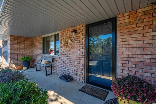 doorway to property with covered porch and brick siding