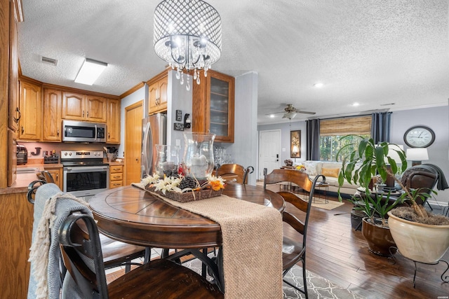 dining space with a textured ceiling, ceiling fan with notable chandelier, wood finished floors, visible vents, and ornamental molding