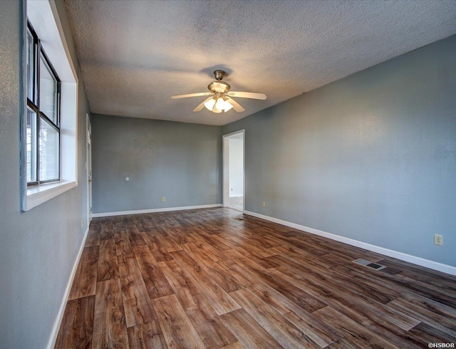 empty room featuring visible vents, baseboards, dark wood finished floors, ceiling fan, and a textured ceiling