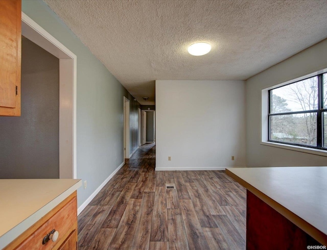 interior space with a textured ceiling, dark wood-style flooring, visible vents, and baseboards