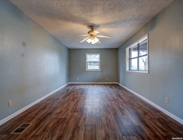 empty room with ceiling fan, dark wood-type flooring, visible vents, and baseboards