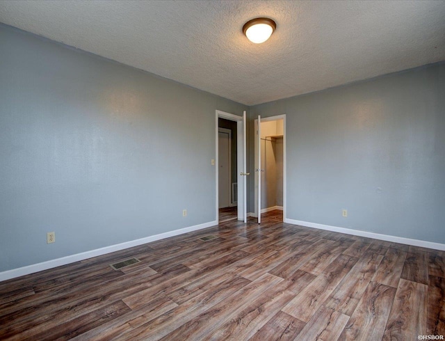 empty room featuring a textured ceiling, dark wood-style flooring, visible vents, and baseboards