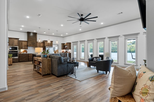 living room featuring visible vents, light wood-style flooring, ceiling fan, and ornamental molding