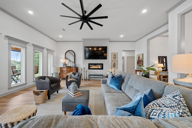 living room with light wood finished floors, recessed lighting, ceiling fan, crown molding, and a large fireplace