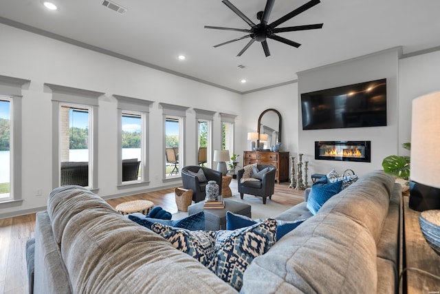 living area featuring wood finished floors, visible vents, plenty of natural light, ornamental molding, and a glass covered fireplace