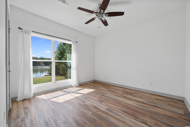 empty room featuring visible vents, baseboards, a water view, wood finished floors, and a ceiling fan