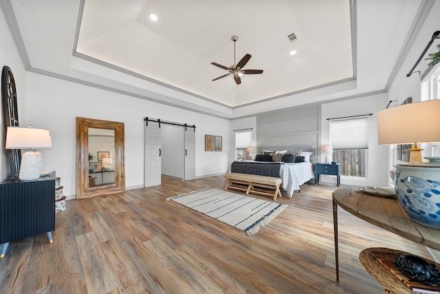 bedroom with visible vents, crown molding, a barn door, wood finished floors, and a raised ceiling