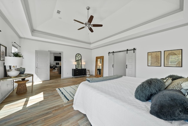 bedroom featuring a tray ceiling, a barn door, wood finished floors, and visible vents