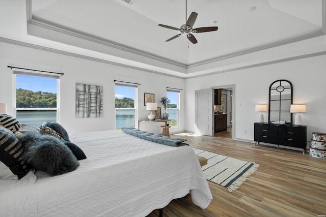 bedroom with a tray ceiling, multiple windows, wood finished floors, and ornamental molding