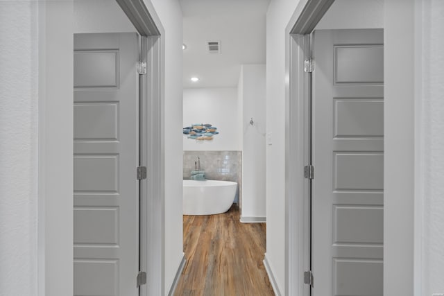 hallway featuring visible vents, tile walls, and wood finished floors