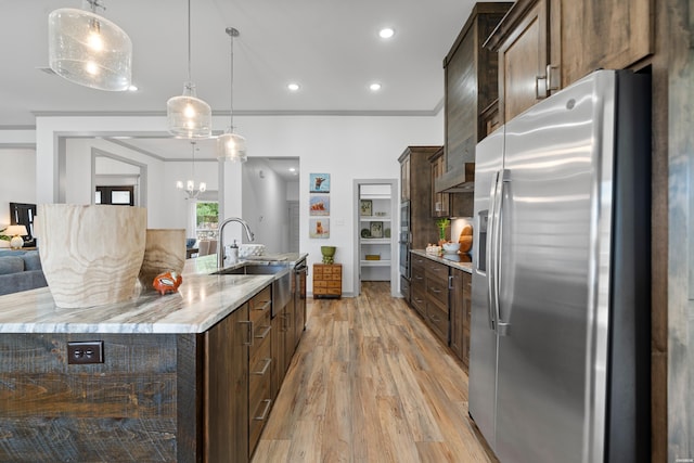 kitchen featuring light wood-type flooring, a sink, hanging light fixtures, dark brown cabinetry, and stainless steel fridge