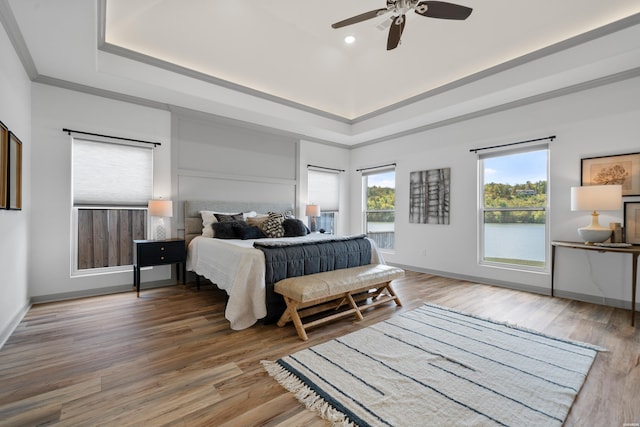 bedroom featuring a tray ceiling, baseboards, wood finished floors, and crown molding