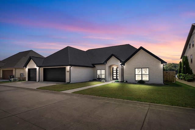 french country style house featuring brick siding, fence, concrete driveway, a lawn, and a garage