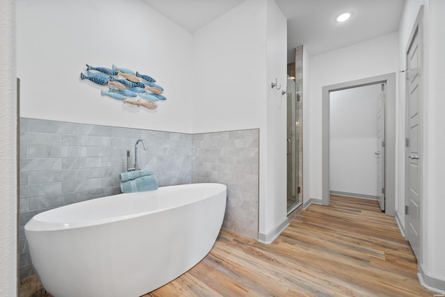 full bathroom with wood finished floors, a wainscoted wall, a freestanding bath, a shower stall, and tile walls