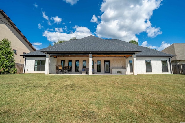 rear view of house featuring brick siding, a lawn, and fence