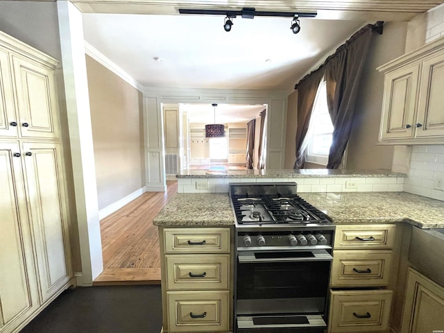 kitchen with stainless steel gas stove, a peninsula, cream cabinetry, and decorative backsplash