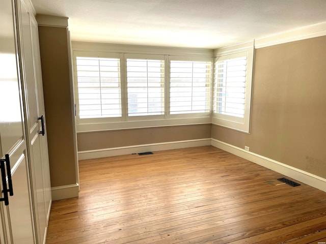 spare room with light wood-type flooring, visible vents, and baseboards