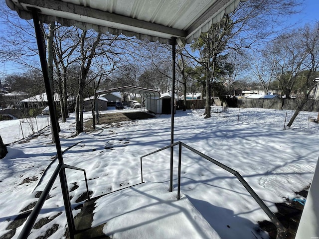 snowy yard featuring a carport and fence