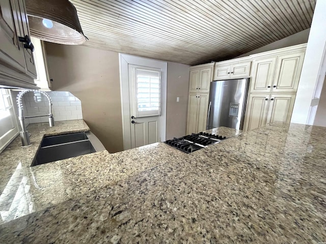 kitchen featuring stainless steel appliances, a sink, decorative backsplash, and light stone counters