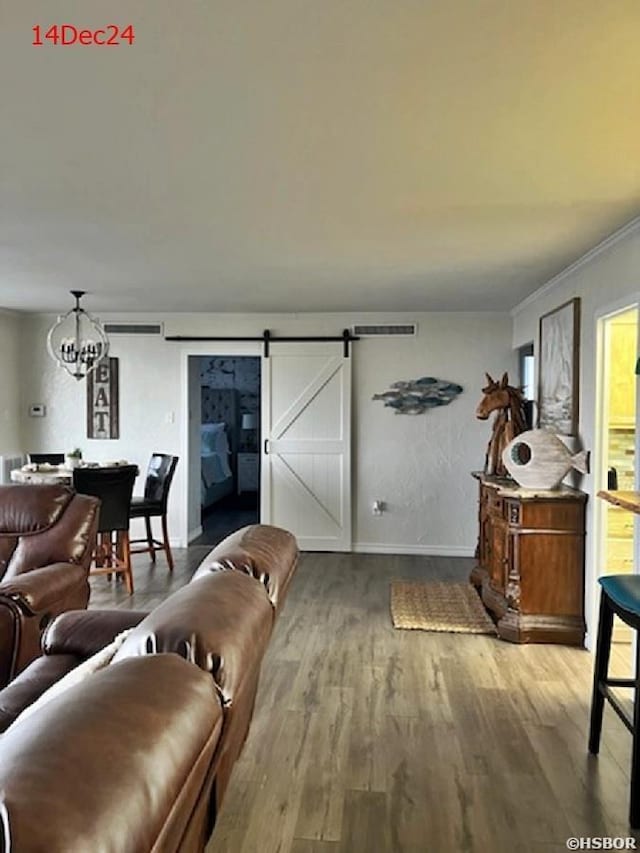 living area featuring a barn door, visible vents, wood finished floors, crown molding, and a chandelier