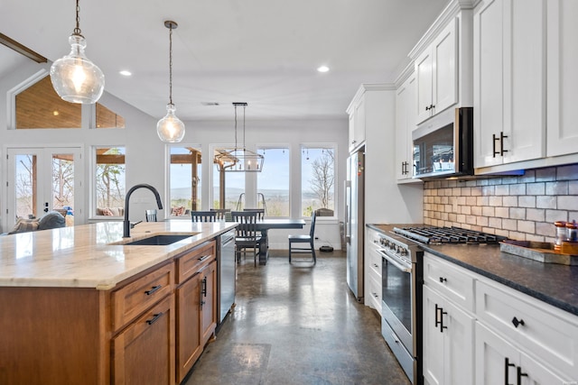 kitchen featuring stainless steel appliances, a sink, white cabinetry, decorative backsplash, and a center island with sink