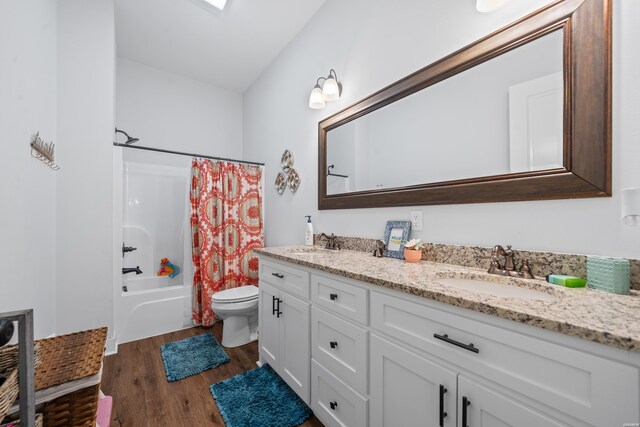 bathroom featuring toilet, double vanity, a sink, and wood finished floors