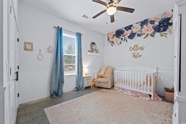 bedroom with a decorative wall, a wainscoted wall, visible vents, finished concrete flooring, and a crib