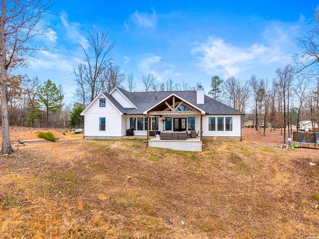 view of front of property featuring a trampoline, roof with shingles, a patio, a chimney, and outdoor lounge area