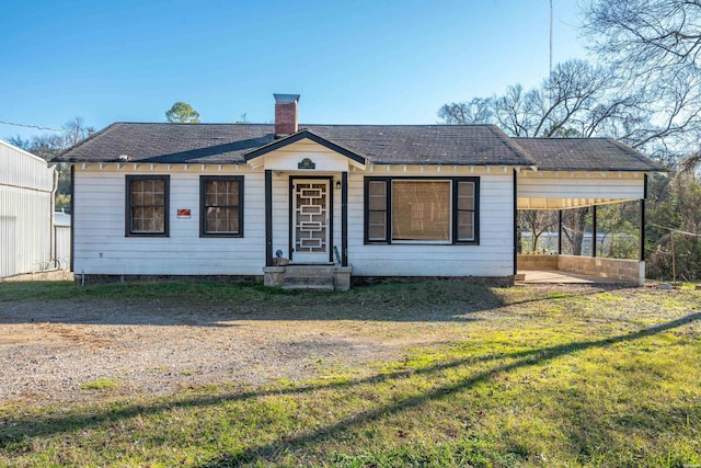 bungalow with dirt driveway, a chimney, and a front lawn