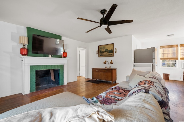 living area featuring a ceiling fan, a tile fireplace, and dark wood-style flooring