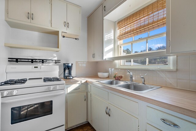 kitchen featuring backsplash, gas range gas stove, light countertops, open shelves, and a sink