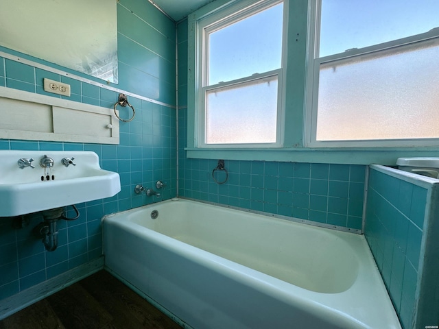 full bath featuring a tub to relax in, a sink, and tile walls