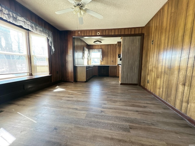 empty room with ceiling fan, wooden walls, dark wood finished floors, and a textured ceiling