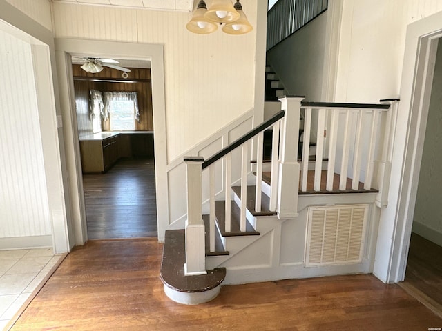 stairway featuring ceiling fan with notable chandelier, wood finished floors, visible vents, and baseboards