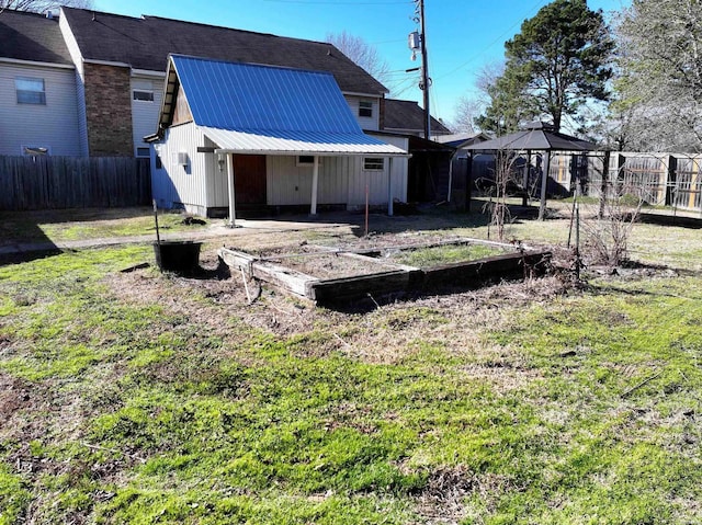 back of house featuring a yard, a gazebo, metal roof, fence, and a garden