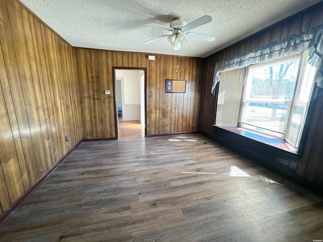 spare room with a textured ceiling, ceiling fan, wooden walls, wood finished floors, and baseboards