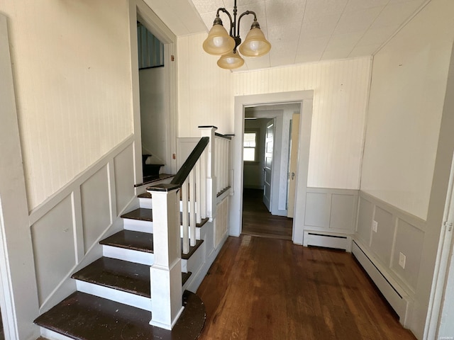 staircase with a decorative wall, baseboard heating, wood finished floors, and an inviting chandelier