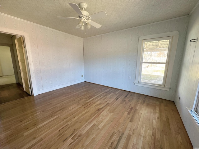 unfurnished room with a ceiling fan, a textured ceiling, ornamental molding, and wood finished floors