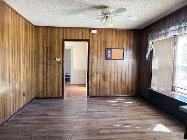 unfurnished room featuring a textured ceiling, wooden walls, wood finished floors, a ceiling fan, and baseboards